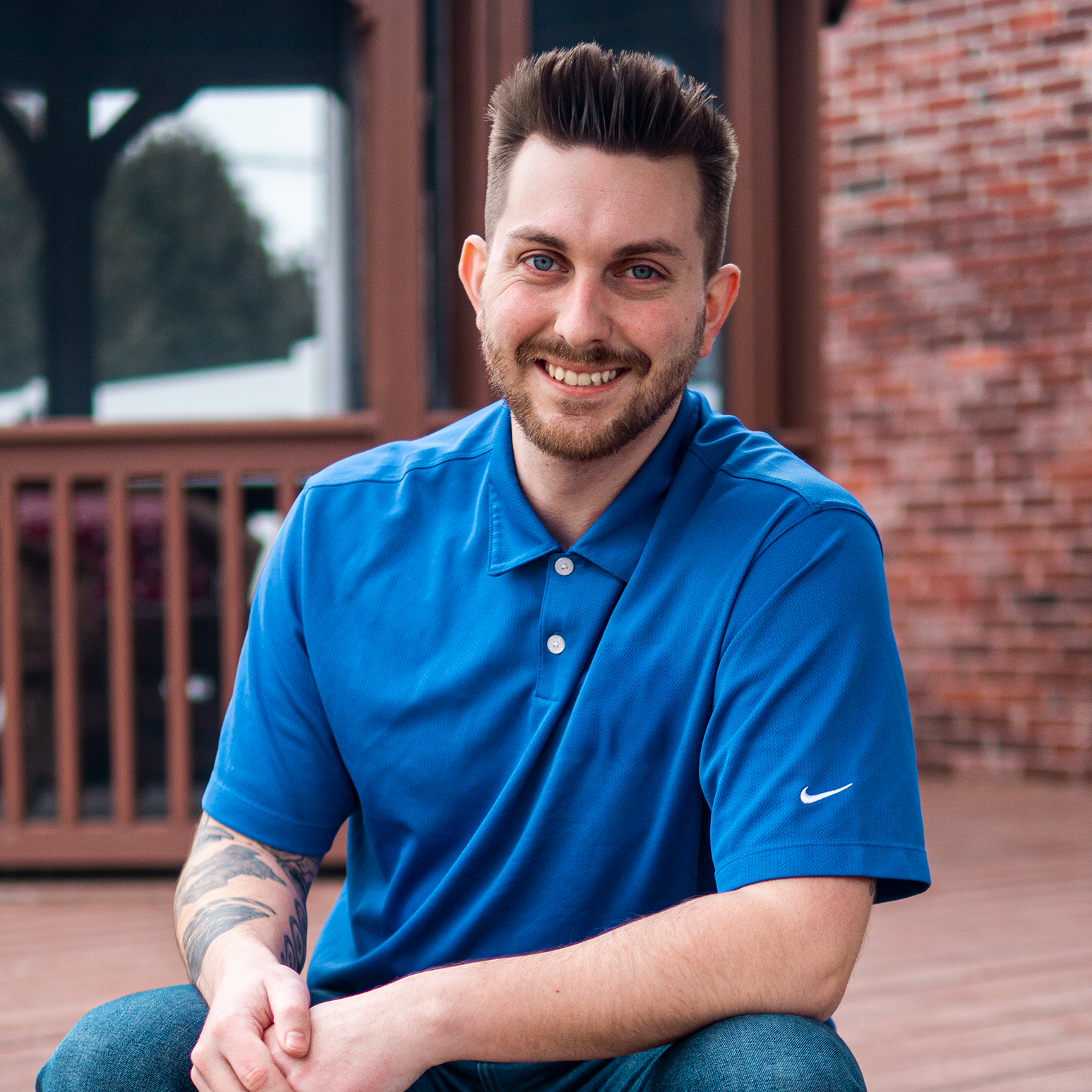 Tyler Hadley smiling and facing the camera in a professional setting, wearing business attire. The background shows a bright office environment. The mood is confident and approachable.